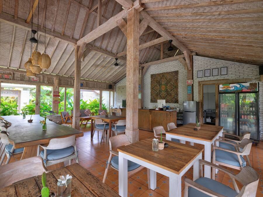 A rustic wooden interior with high ceilings and large windows. Tables and chairs are arranged for dining.