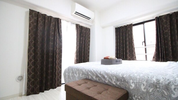 A hotel room with a large bed, a bench, and an air conditioning unit. - Narimasu Apartment 12 (Tokyo)
