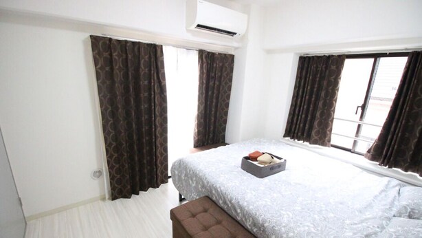 A bedroom with a bed, a bench, a bedside table, and a window with curtains. - Narimasu Apartment 21 (Tokyo)