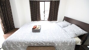 A bedroom with a large bed, a bedside table, a window with curtains, and a small bedside table with a lamp. - Narimasu Apartment 21 (Tokyo)