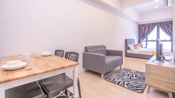 Una habitación de hotel moderna con una mesa de comedor de madera, un sofá gris y una cama con cabecera gris.