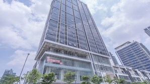 Un edificio moderno de gran altura con fachada de vidrio, un cartel visible que dice 'RENT' y la infraestructura urbana circundante.