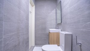 Un baño pequeño con azulejos grises, un inodoro blanco, un mueble de madera y un espejo en la pared.