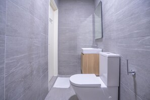 Un baño pequeño con azulejos grises, un inodoro blanco, un mueble de madera y un espejo en la pared.
