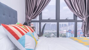 Habitación de hotel con un ventanal grande, una cama con almohadas coloridas y un ordenador portátil sobre la mesita de noche.