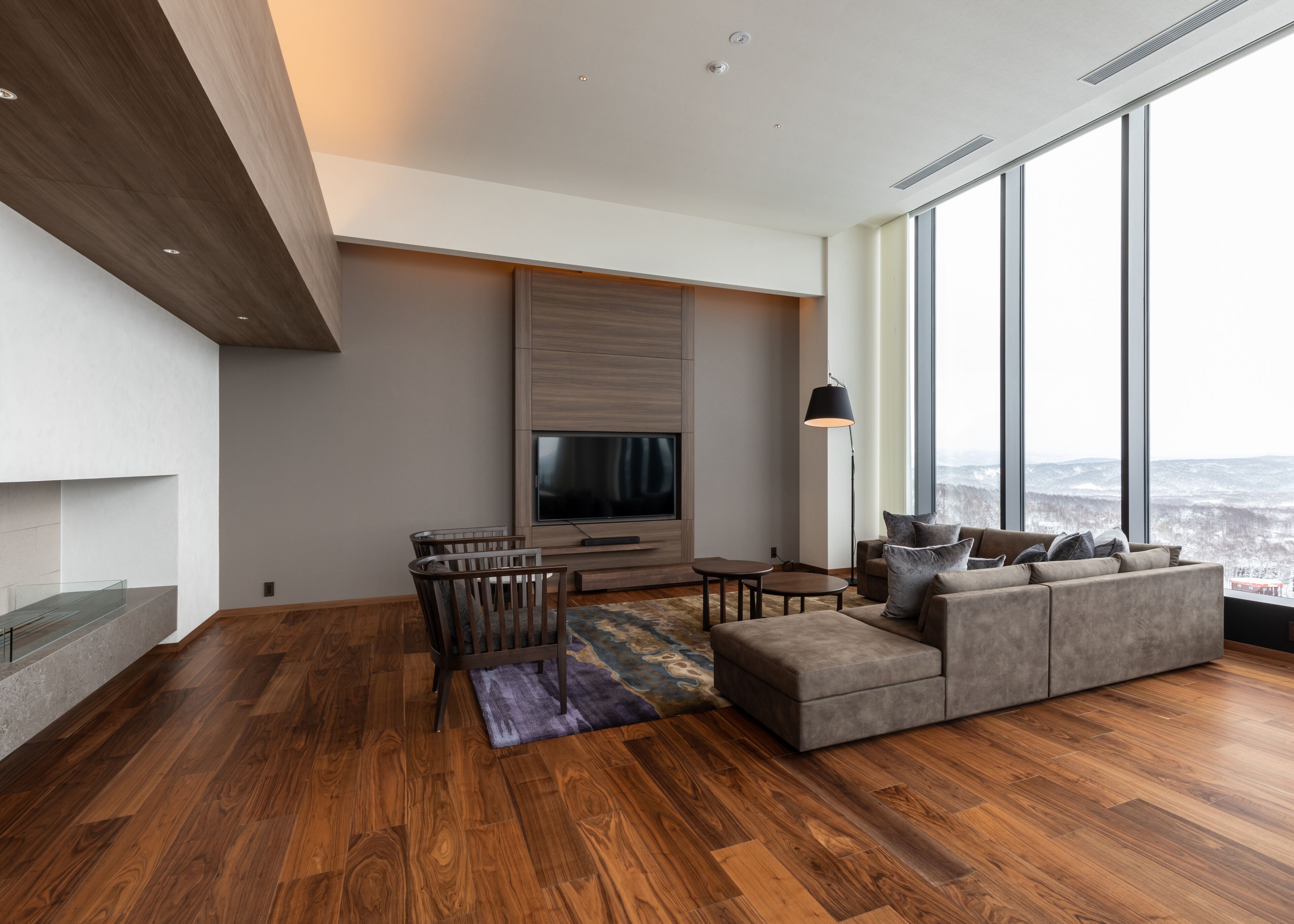A modern living room with a large TV, comfortable seating, and a view through large windows.