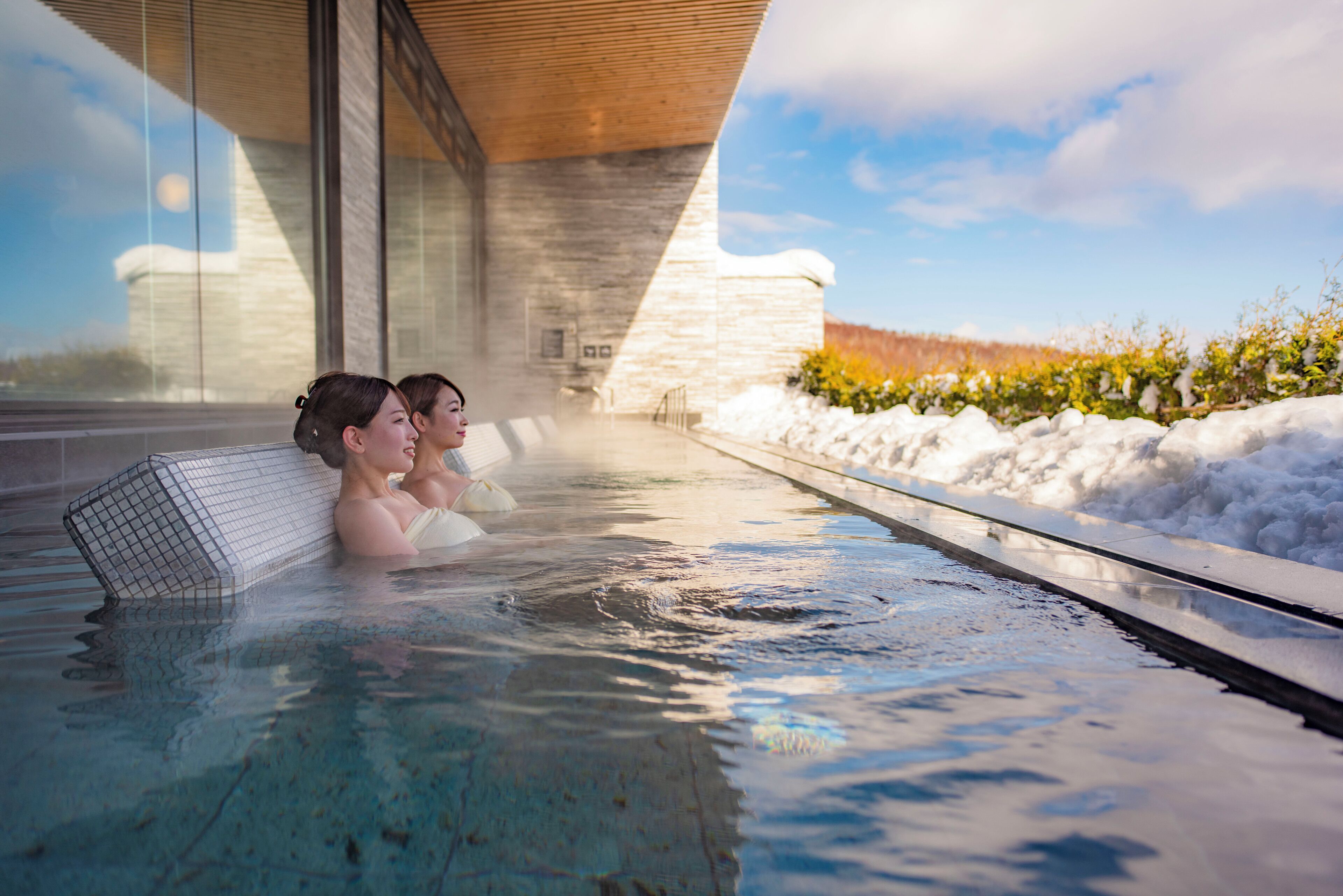Un jacuzzi con dos personas, una pared de piedra y un paisaje nevado.
