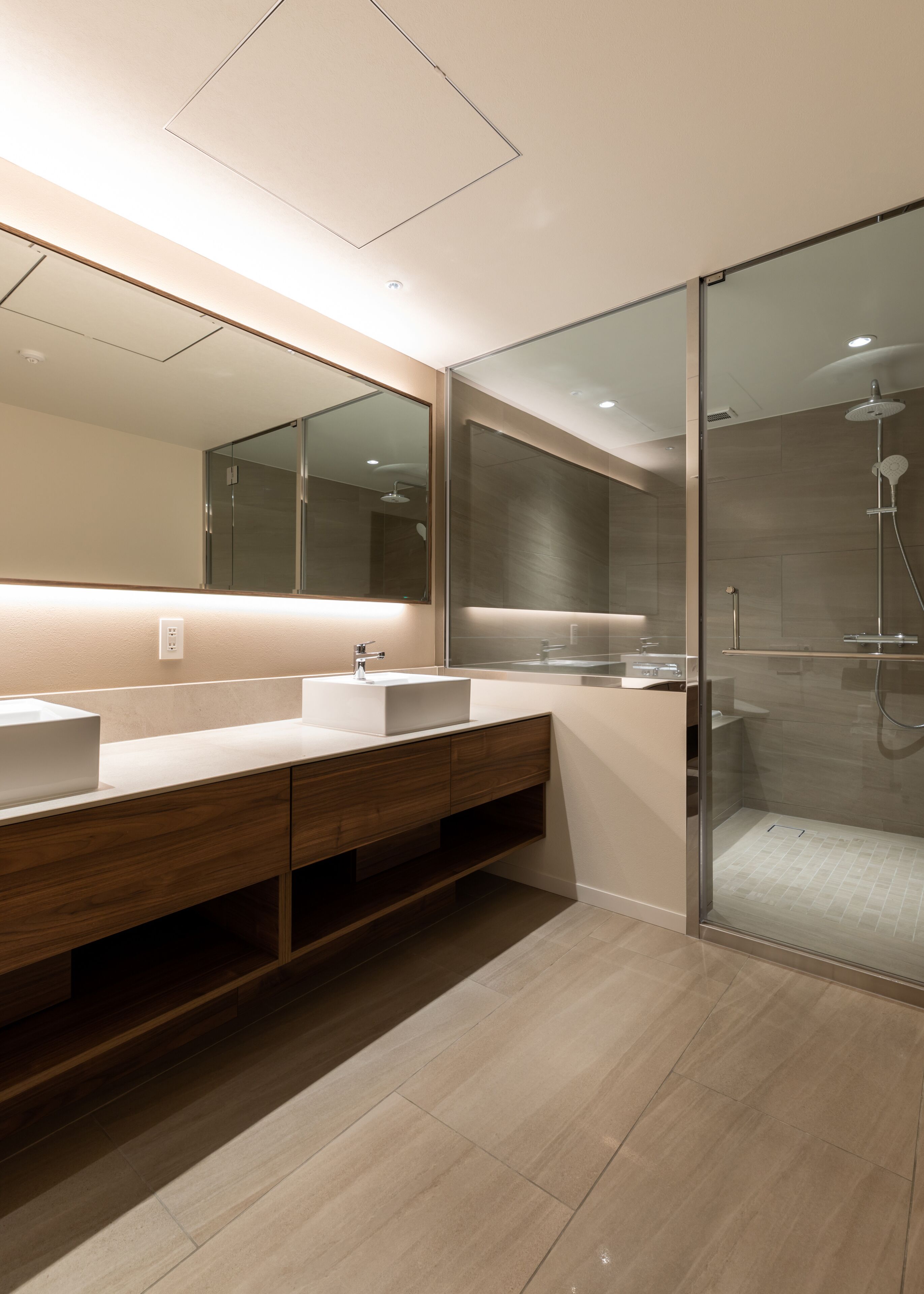 A modern bathroom with a large mirror, two sinks, wooden vanity, and a glass-enclosed shower area.