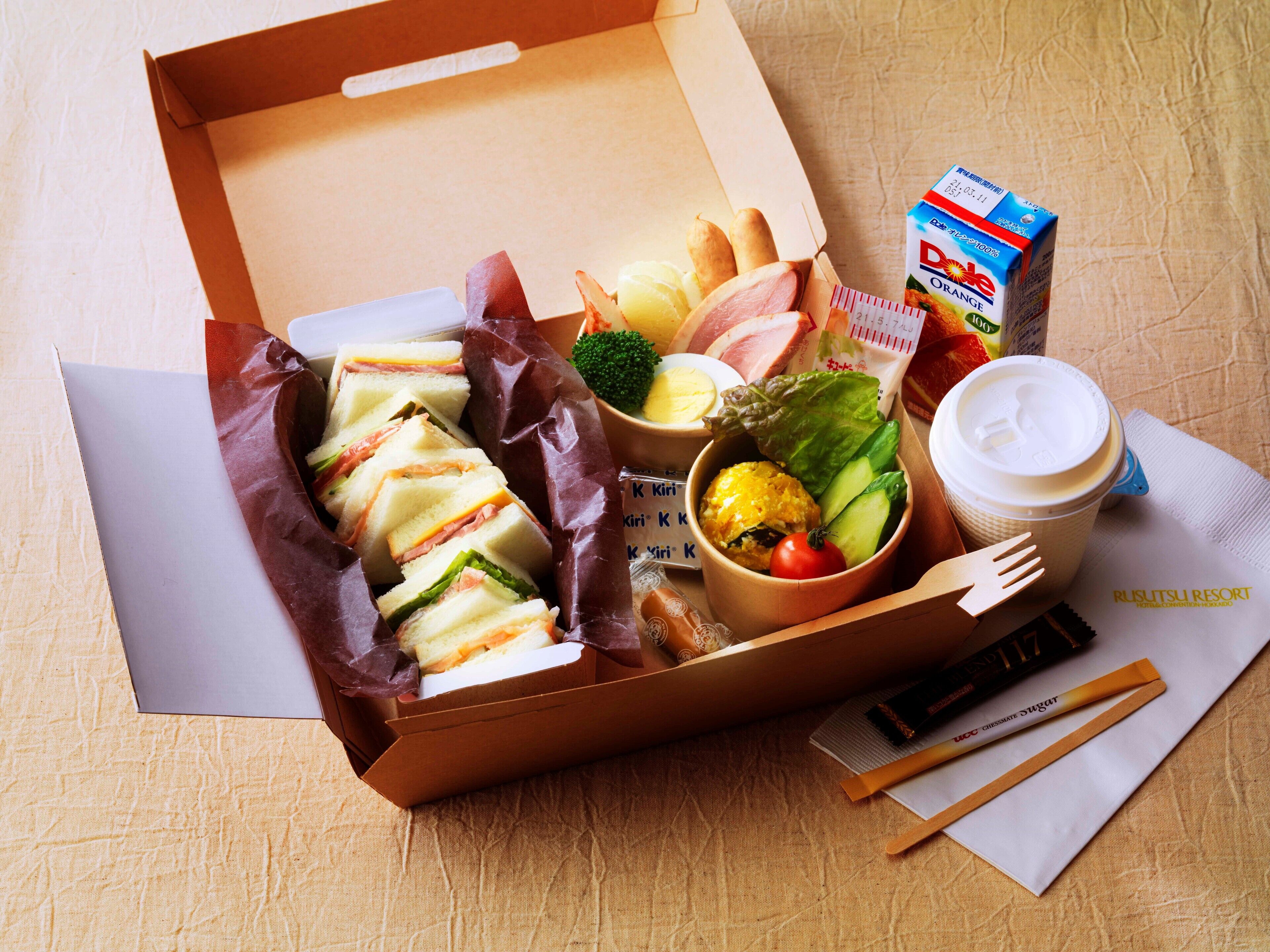 Een maaltijdbox met belegde broodjes, een salade, een kop koffie en een vruchtensap.