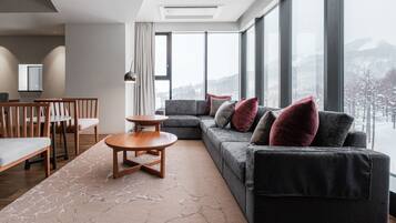 A modern living room with a grey sofa, wooden coffee table, and a view of a snowy landscape through large windows.