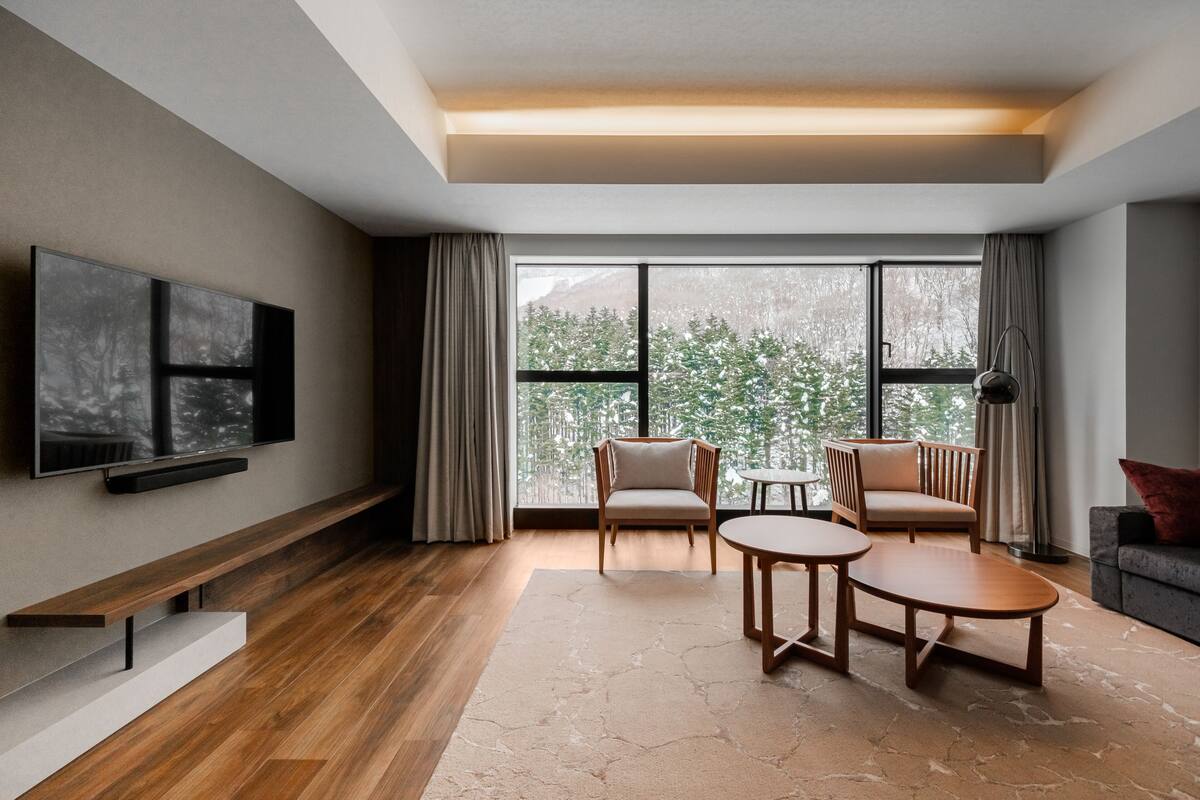A modern living room with a large window, a flat-screen TV, a wooden bench, and a sofa.