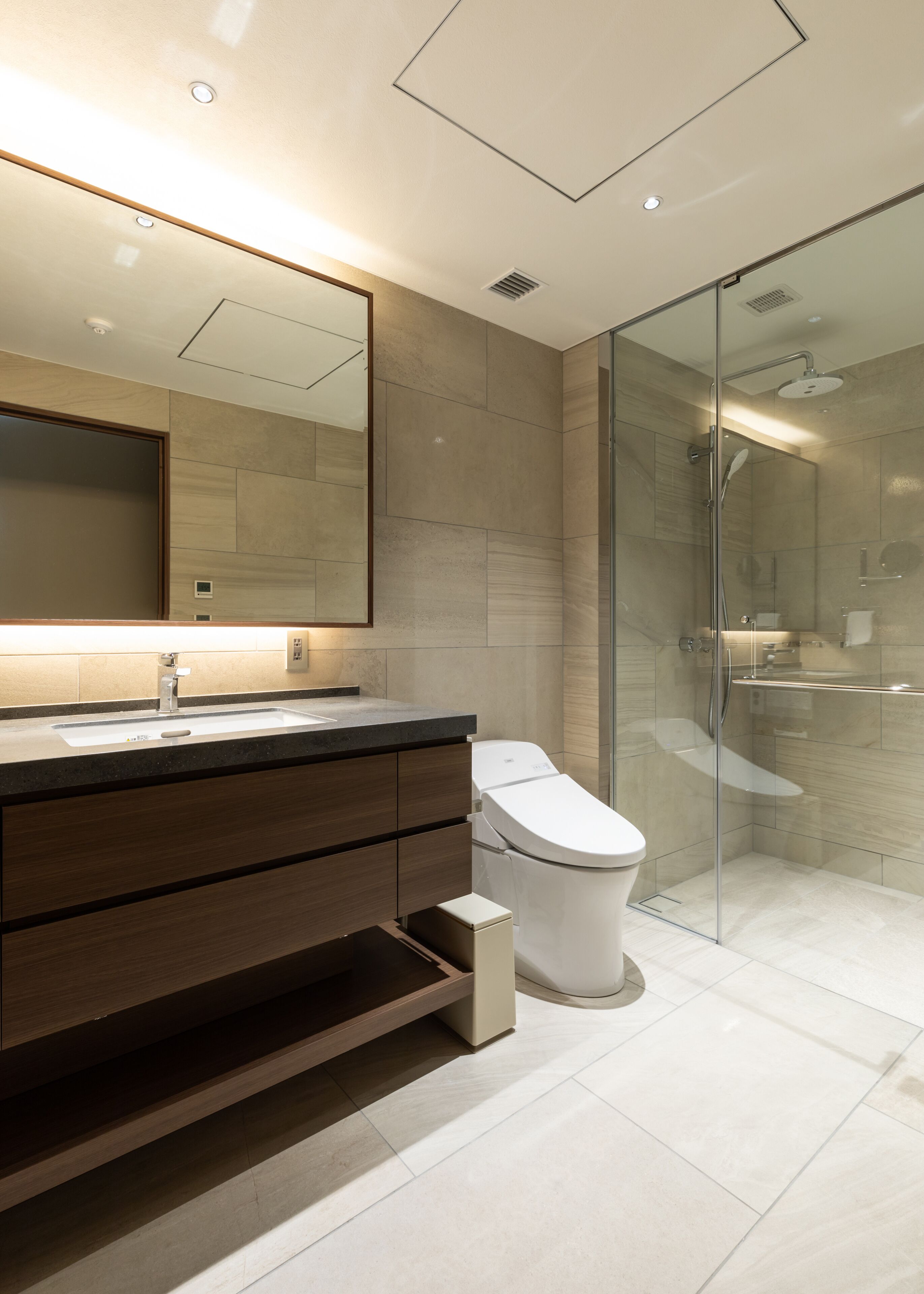 A modern bathroom with a large mirror, a sink, a toilet, and a glass-enclosed shower area.