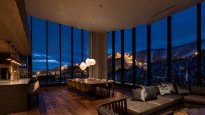 A modern interior with a large dining area, a sofa, and a view of a snowy landscape through large windows. - The Vale Rusutsu (Rusutsu)