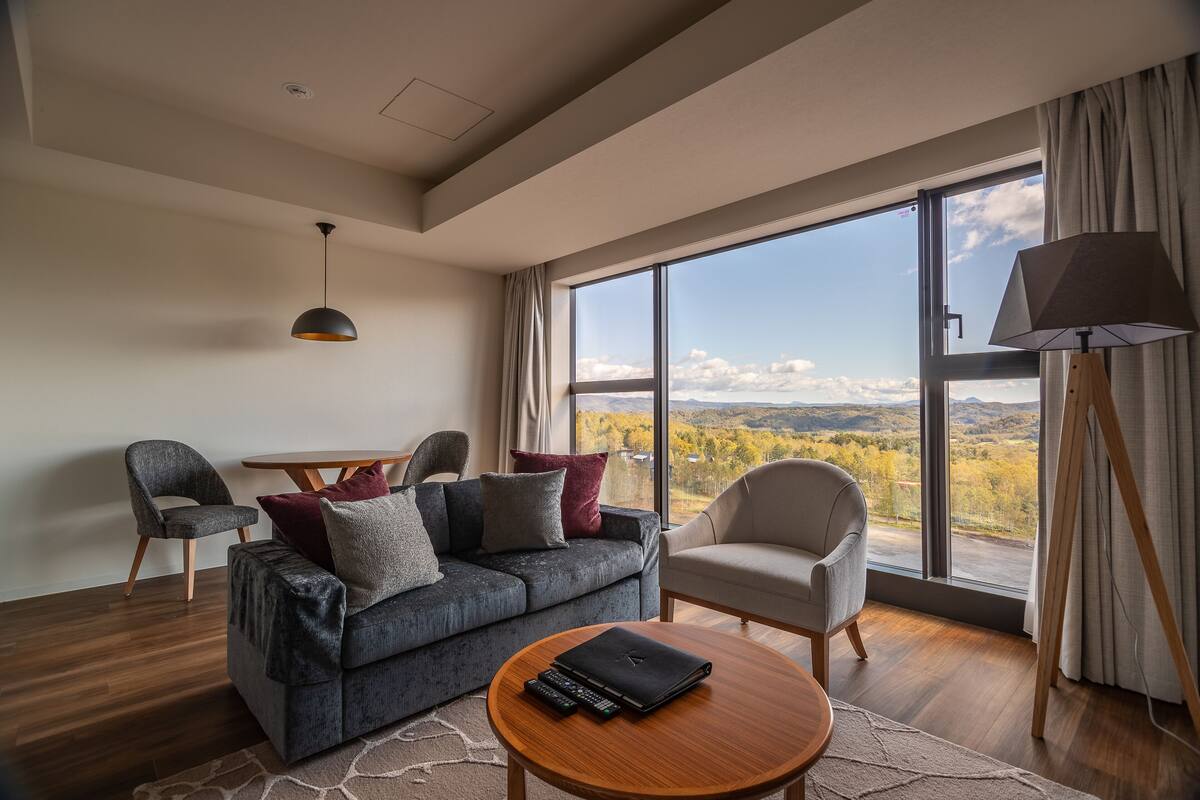 A modern living room with a sofa, chairs, a coffee table, and a view of a mountainous landscape through large windows.