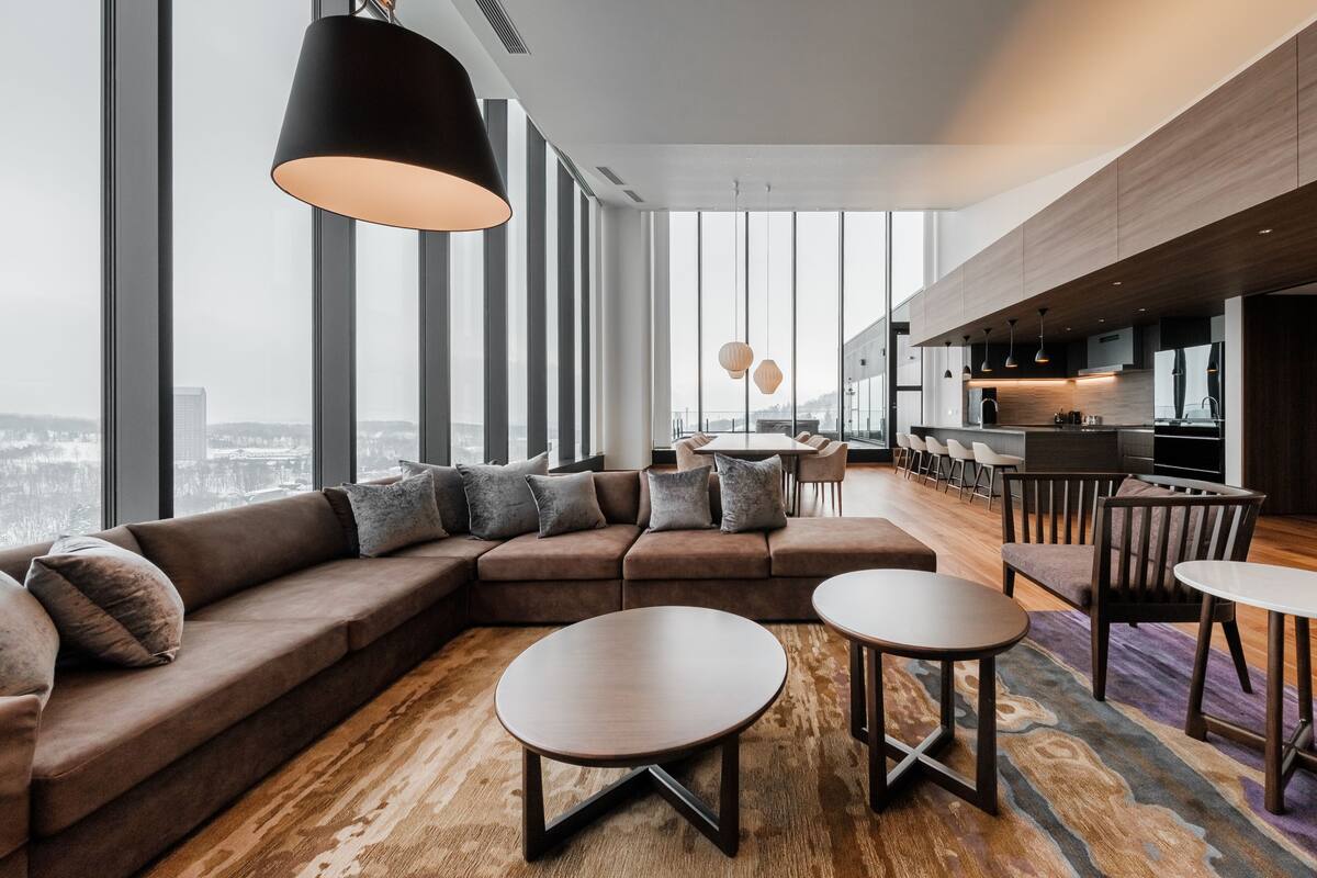 A modern living area with a large sectional sofa, round coffee tables, and a city view through large windows.