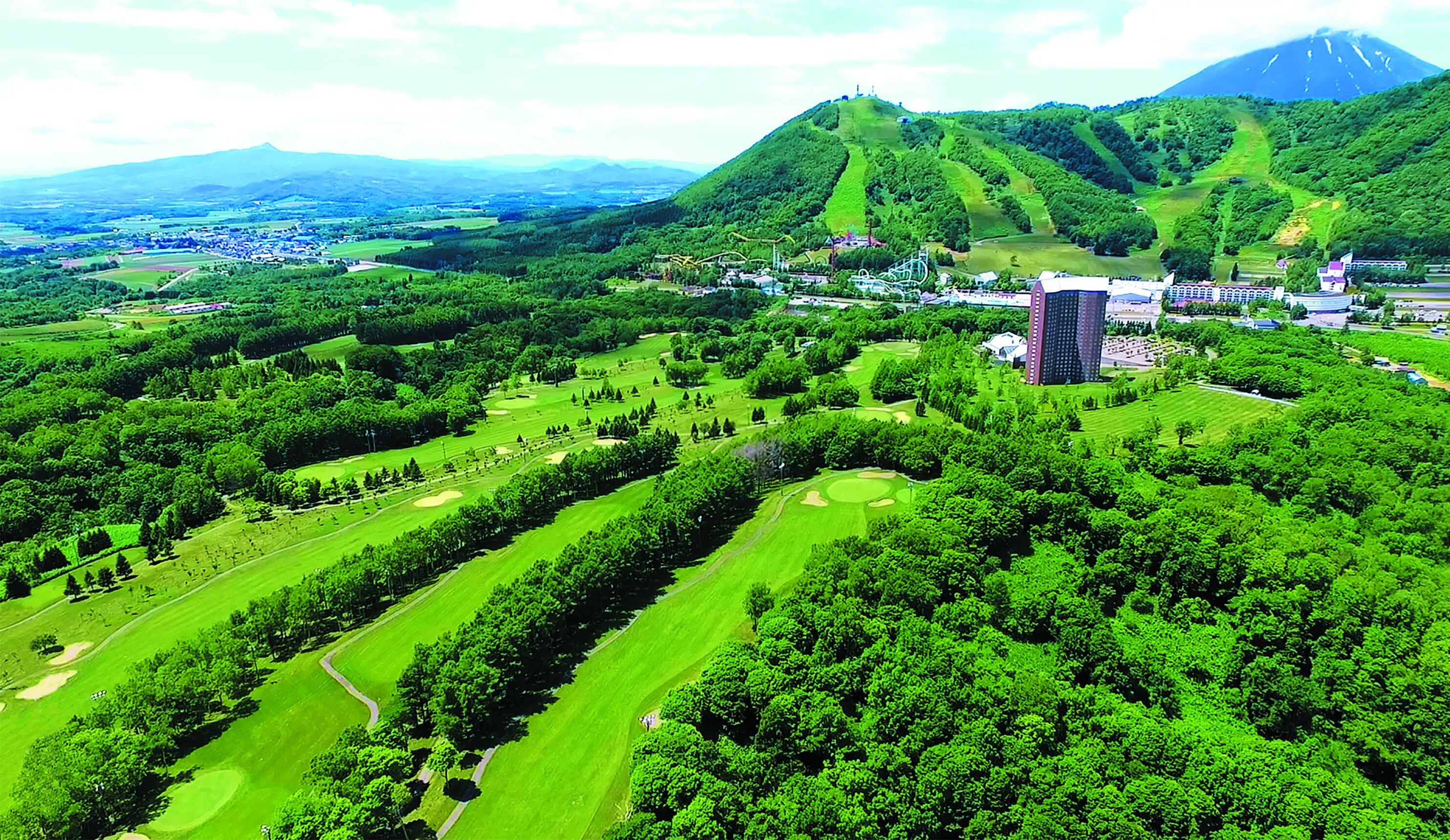 Um campo de golfe com um edifício grande e uma montanha ao fundo.