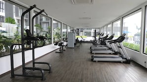 A gym with exercise equipment, large windows, and a view of buildings. - Happy Home Inn Sdn Bhd (Iskandar Puteri)