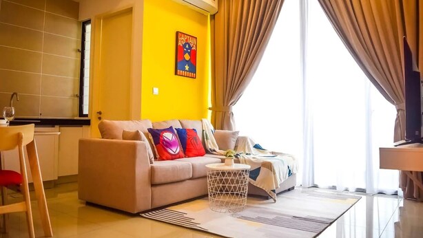 A modern living room with a sofa, a coffee table, and a dining area with a chair and a small table. - Happy Home Inn Sdn Bhd (Iskandar Puteri)