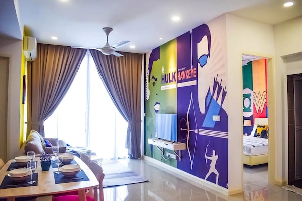 Una habitación de hotel moderna con zona de comedor, un amplio ventanal con cortinas, un ventilador de techo y un mural colorido en la pared.