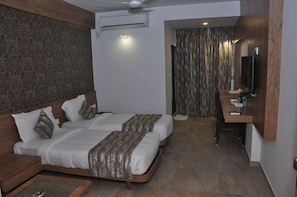 A hotel room with two beds, a desk, a TV, and a ceiling fan.