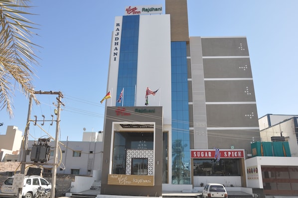 A hotel named Rajdhani with a modern facade, flags, and a visible entrance.