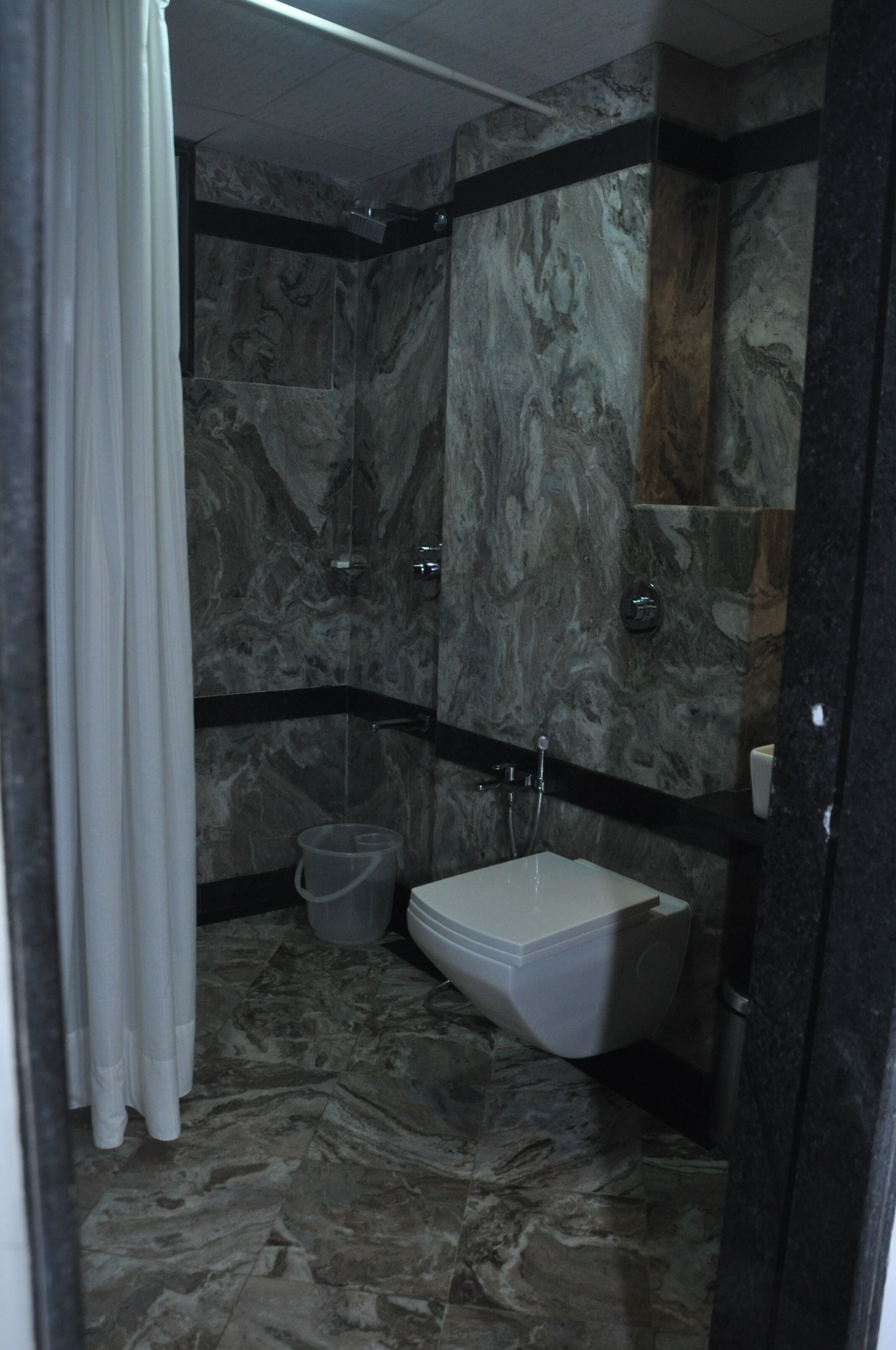 A bathroom with a marble floor, a white toilet, and a shower area.