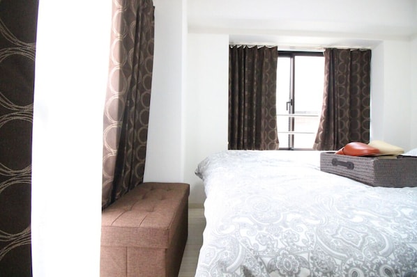 Una habitación de hotel con una cama grande, un banco y una maleta en el suelo.