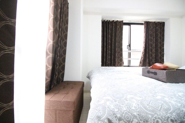 A hotel room with a large bed, a bench, and a suitcase on the floor.