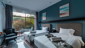 A modern hotel room with two beds, a sofa, a desk, and a balcony with a view of trees. - Begonia Resort (Panglao)