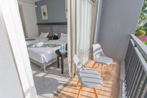 A balcony with two white chairs and a bed with white linens.