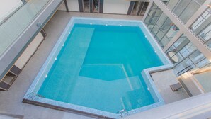 A modern indoor swimming pool with clear blue water, surrounded by glass walls and a tiled floor. - Begonia Resort (Panglao)