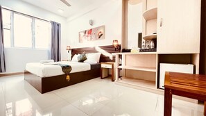 Quarto de hotel moderno com uma cama grande, uma mesa de trabalho e uma cozinha compacta.