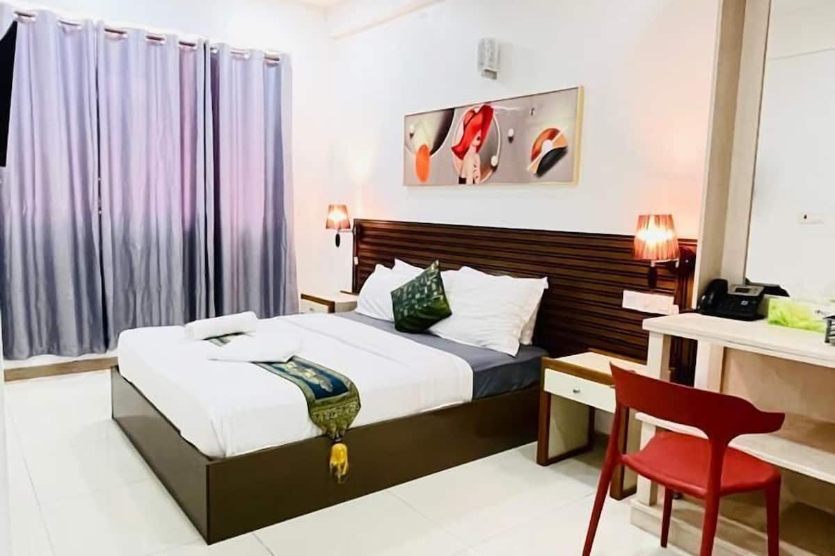 A hotel room with a bed, a desk, a chair, a ceiling fan, and a large mirror.