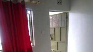 A bedroom with a bed, a window with red curtains, and a door leading to another room.