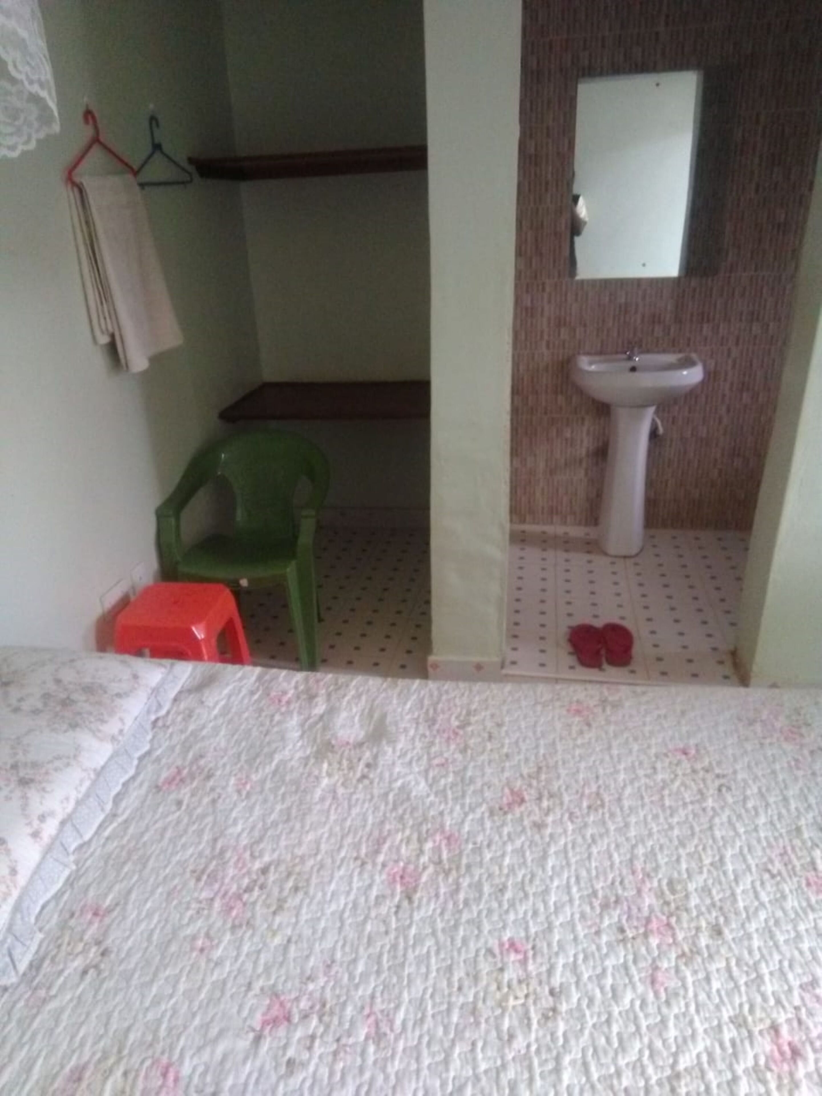 Un dormitorio con una cama, una silla verde, un taburete rojo, un lavabo y un espejo.