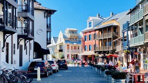 A street lined with colorful buildings, parked cars, and outdoor seating areas. - FlipFlopsOn II • 80 Steps to the Beach • FL 30A • Gulf Coast (Inlet Beach)