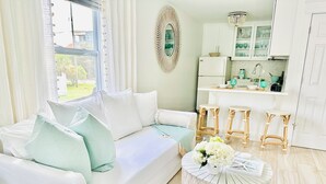 A modern living room with a white sofa, a round woven coffee table, and a kitchen area with white cabinets and bar stools. - FlipFlopsOn II • 80 Steps to the Beach • FL 30A • Gulf Coast (Inlet Beach)