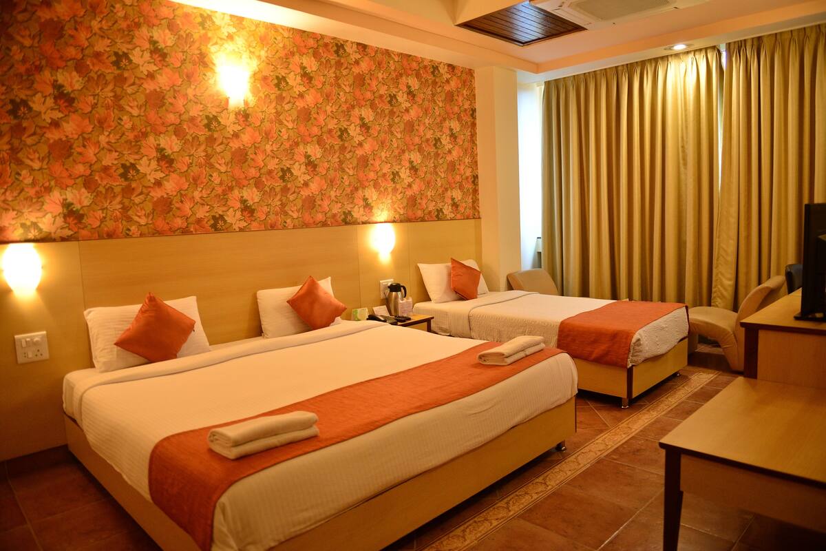 A hotel room with two beds, a sofa, a TV, and a floral wallpaper.