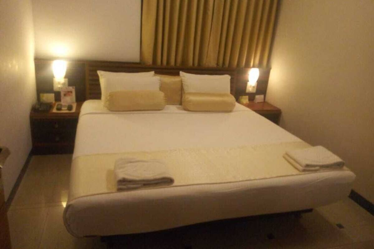 A hotel room with a large bed, two bedside tables, and a curtain.