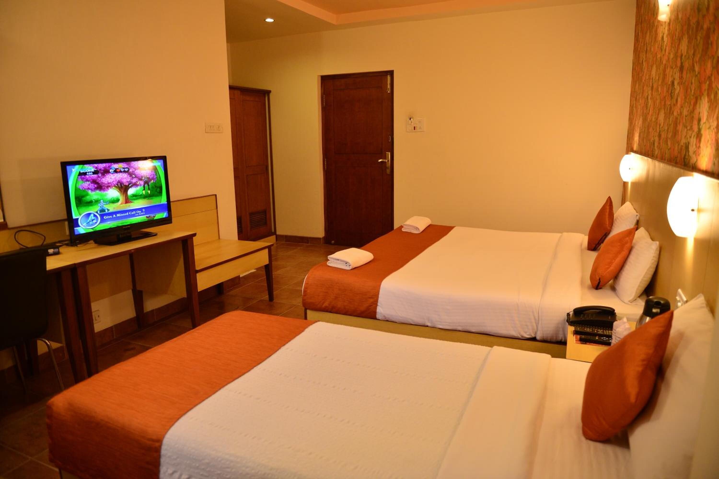 Una habitación de hotel con dos camas, un escritorio y una televisión, y una puerta.