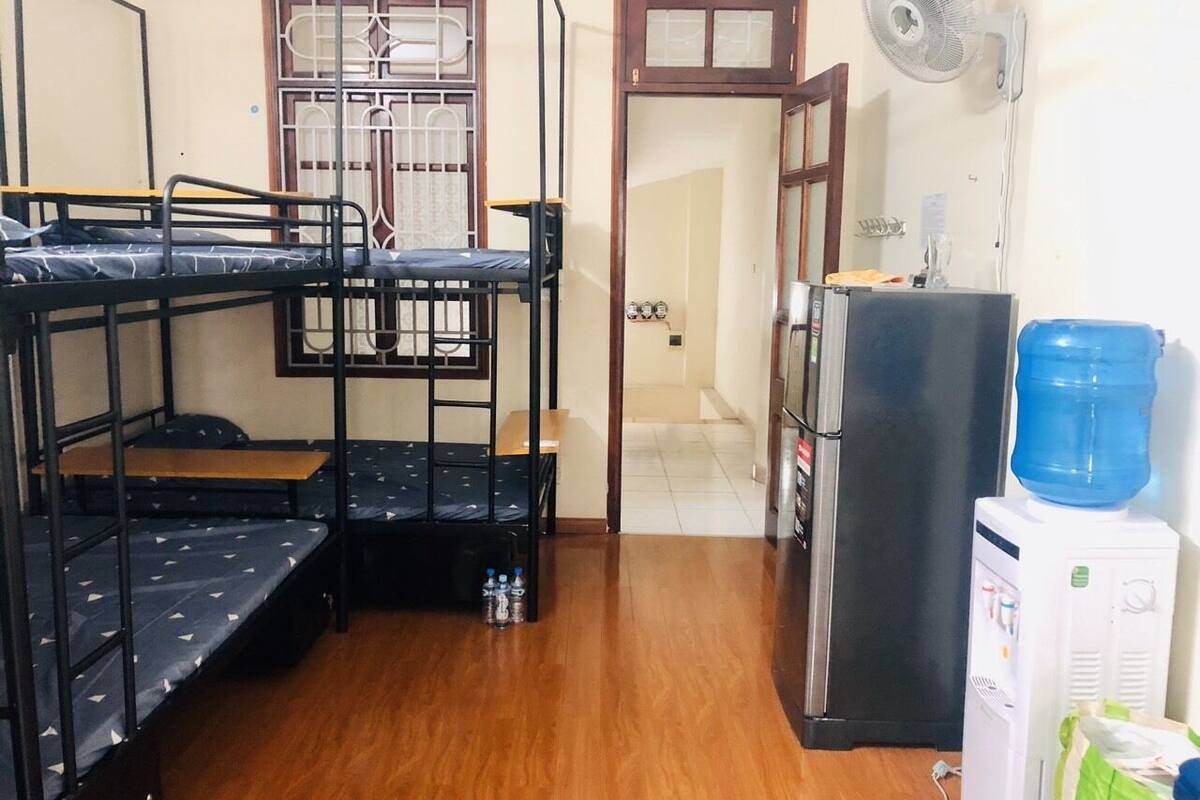 A dormitory room with bunk beds, a refrigerator, a water dispenser, and a fan.
