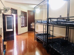 A dormitory room with bunk beds, a wardrobe, a fan, and a door with a window.