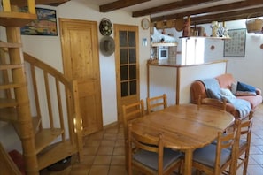 A wooden dining table with chairs, a wooden staircase, a kitchen area with a stove, and a sofa.
