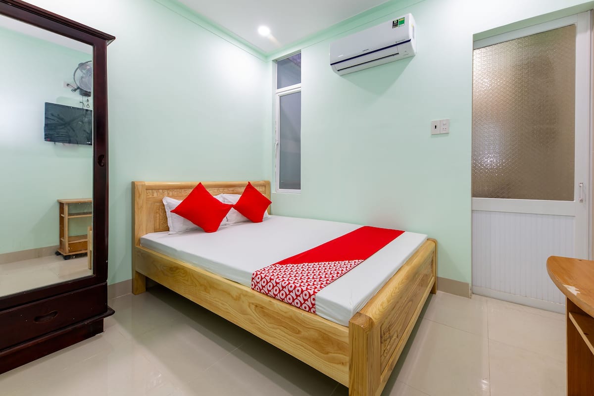 Une chambre à coucher avec un lit en bois, un miroir, un climatiseur et une porte dotée d’un panneau en verre dépoli.