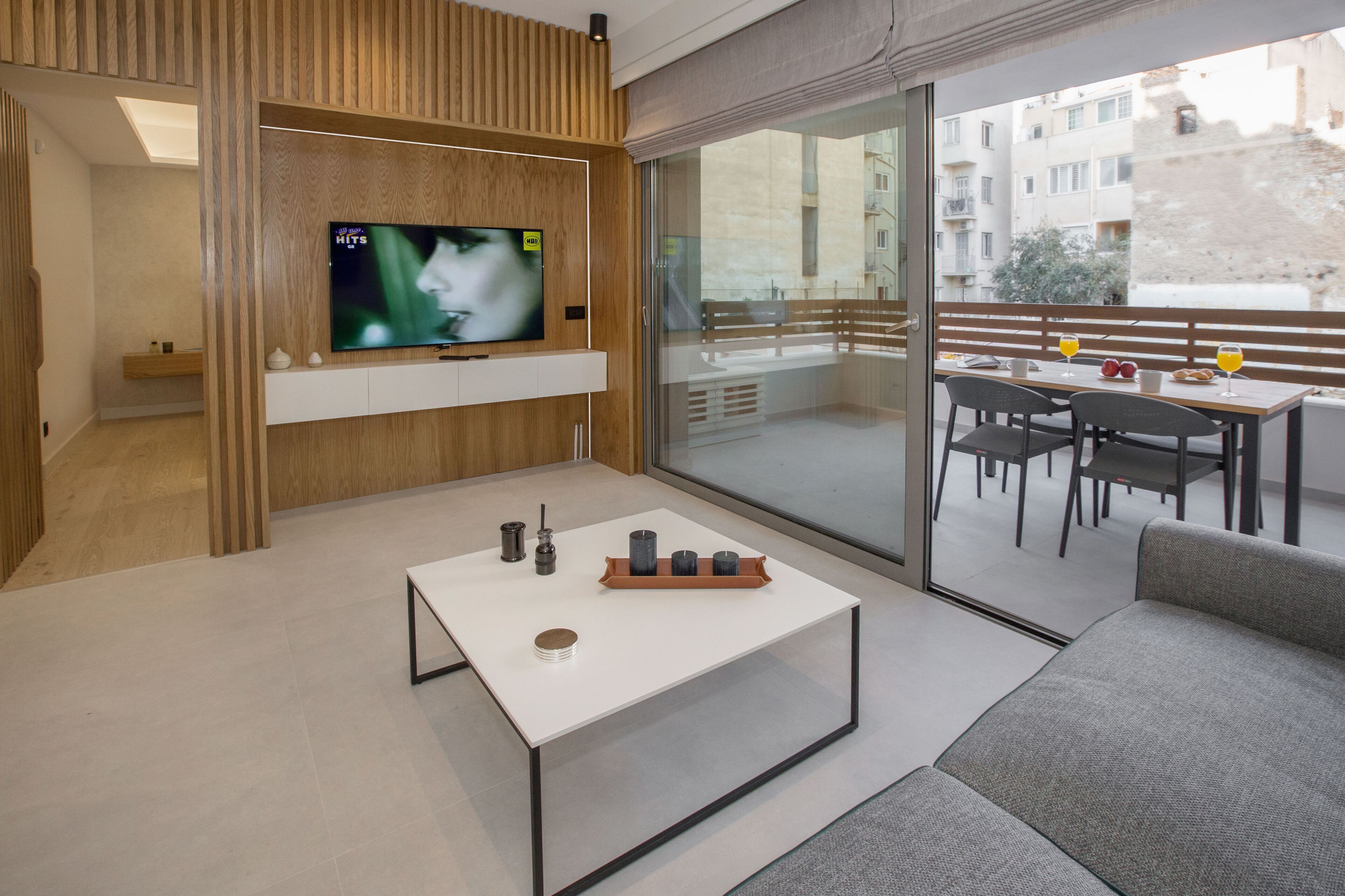 Ein modernes Wohnzimmer mit Flachbildfernseher, Couchtisch und Balkon mit Essbereich.