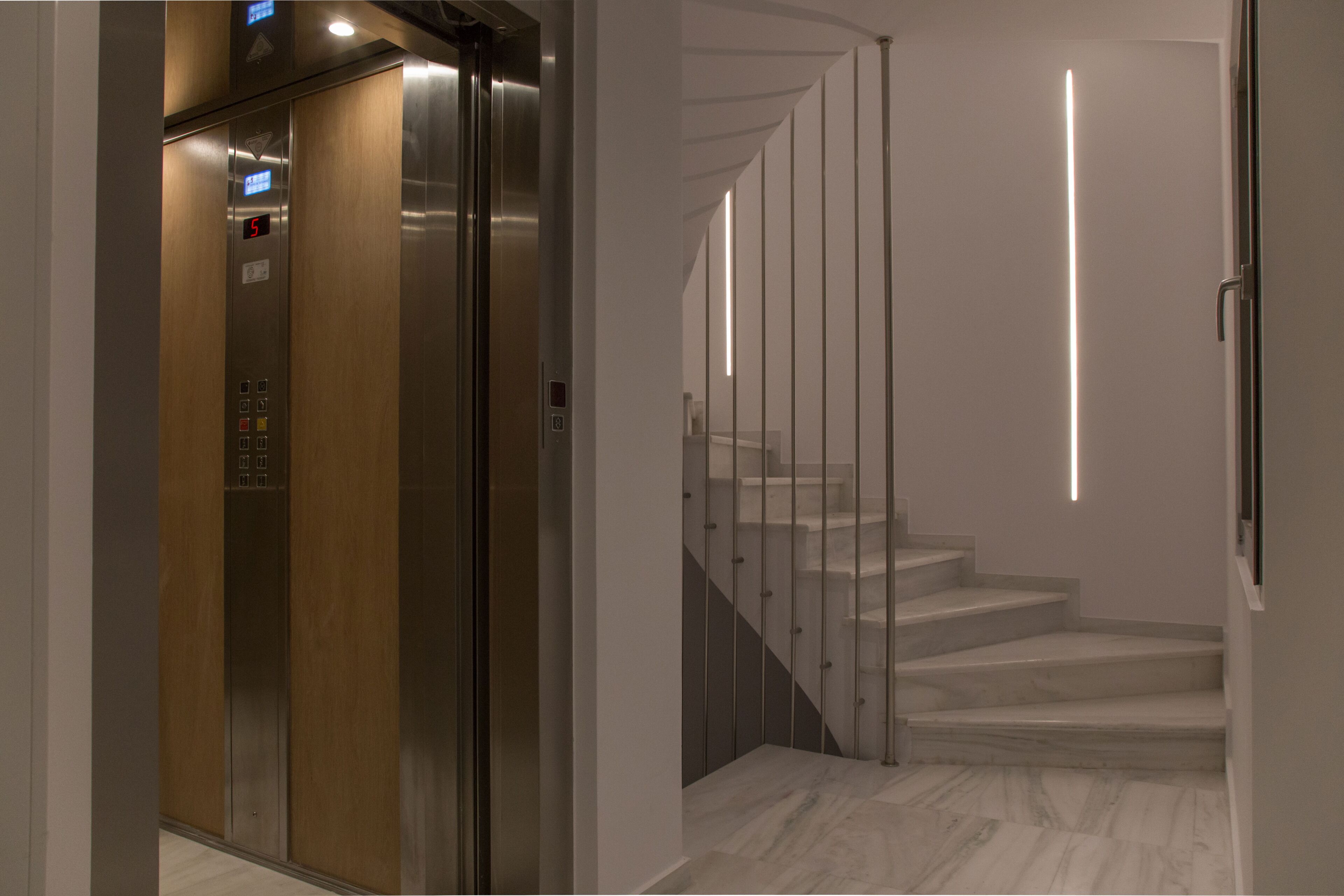 An elevator with a digital display, a staircase with a modern railing, and a marble floor.