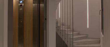 An elevator with a digital display, a staircase with a modern railing, and a marble floor.