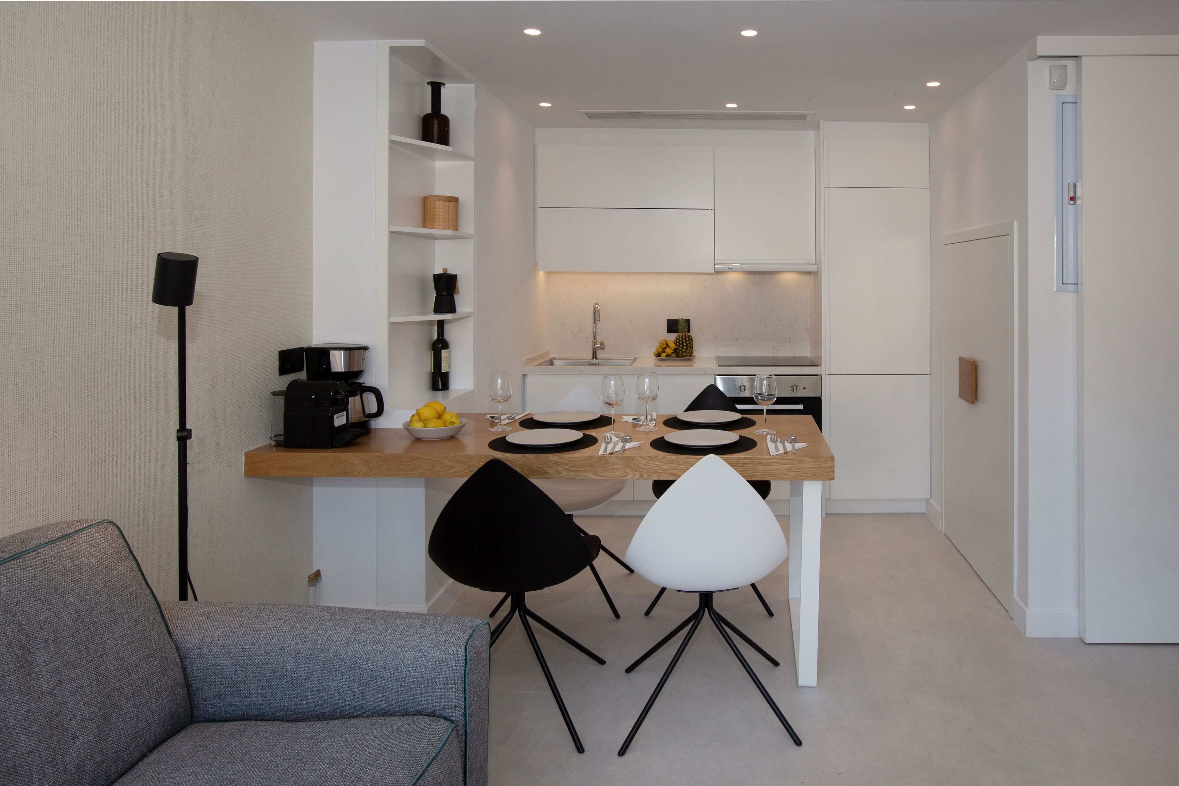 A compact kitchen with white cabinets, a coffee machine, and a dining area with two chairs.