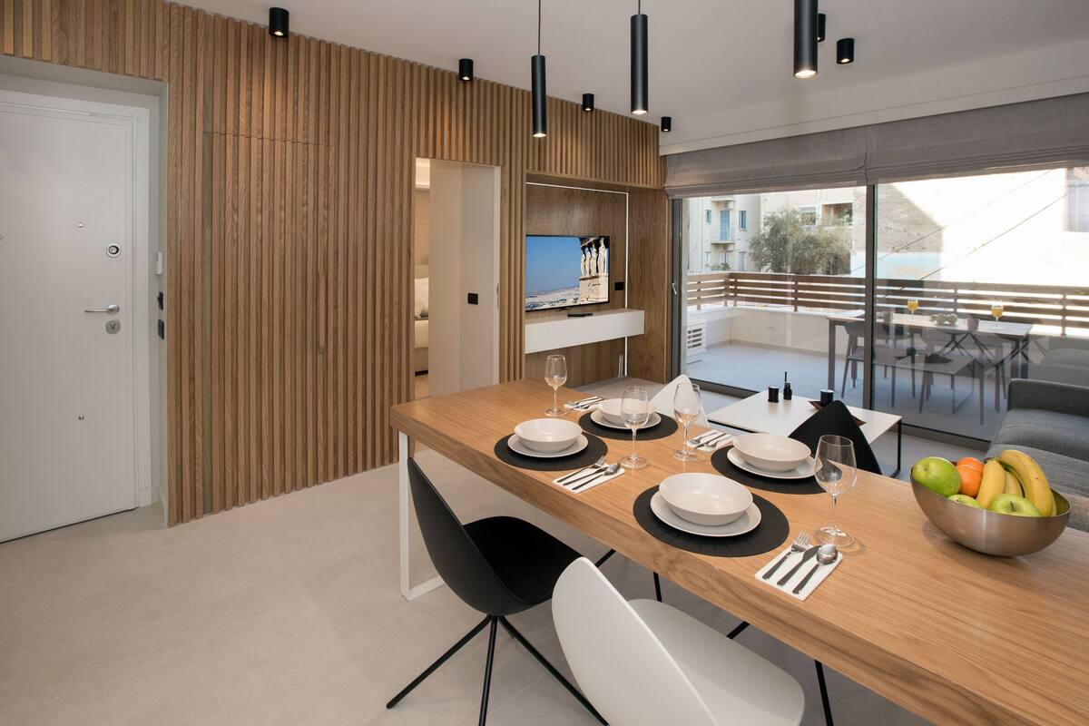 A modern dining area with a wooden table, black chairs, and a fruit bowl.