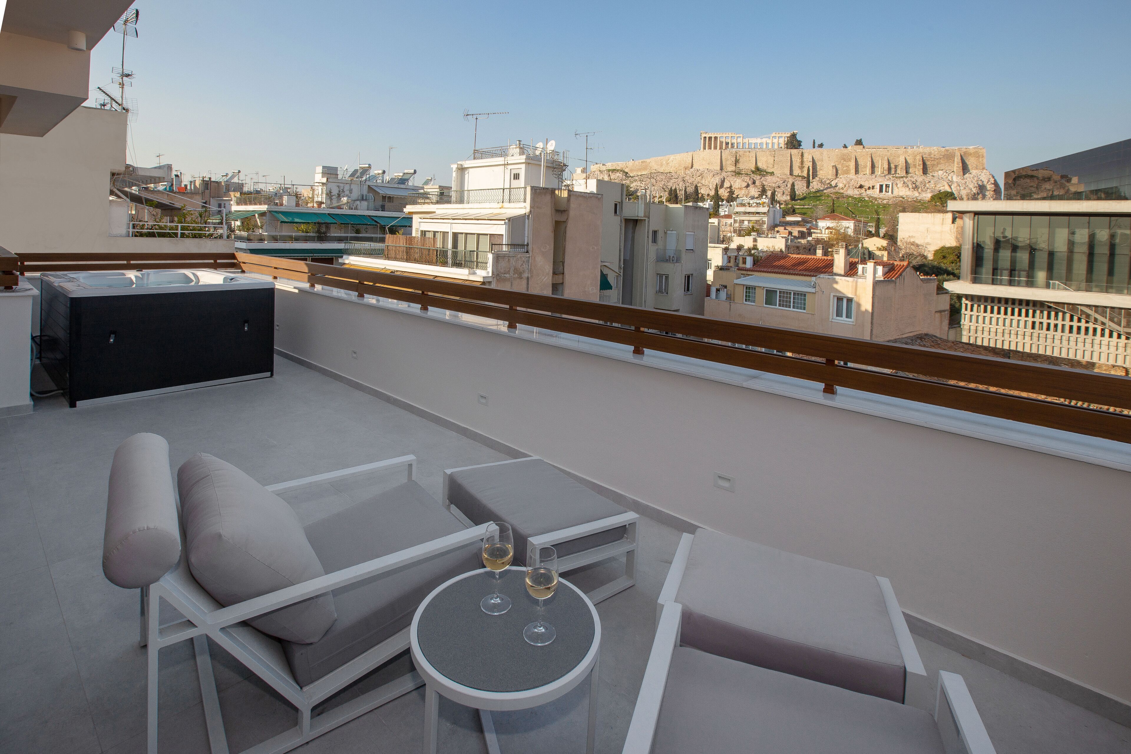 A rooftop terrace with a seating area, a small table, and a view of the cityscape and ancient ruins in the background.